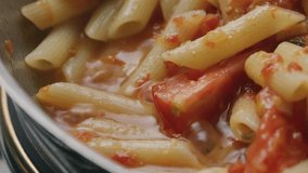 Extreme close-up view of cooking penne pasta with rich tomato sauce in hot pan, stirring ingredients and mixing flavors - Powered by Shutterstock - Get 15% off with code: PIKWIZARD15