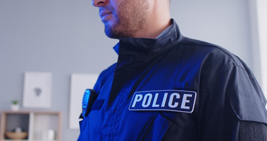 Close up portrait of a confident police officer talking by walkie talkie in flashing lights. Young policeman in uniform standing indoors. Crime and robbery concept. 4k video. Slow motion video.