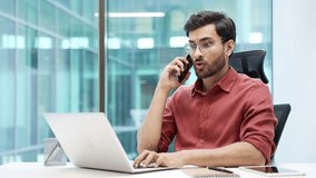 Confident manager talking on phone while sitting at workplace in modern office. Handsome bearded businessman in glasses communicates with a client, or conducts a conversation with a business partner - Powered by Shutterstock - Get 15% off with code: PIKWIZARD15