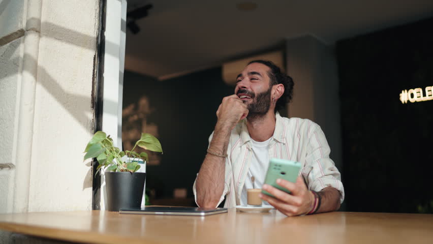 Smiling man using online banking app on smartphone, managing payments and transactions while seated at café. relaxed atmosphere highlights convenience, technology, seamless financial management on go - Powered by Shutterstock - Get 15% off with code: PIKWIZARD15