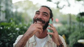 Hispanic man laughing on phone call, while sitting in sidewalk city cafe. Ease of connection enabled by 5G technology. Faster data speeds and communication quality,  connections between people - Powered by Shutterstock - Get 15% off with code: PIKWIZARD15