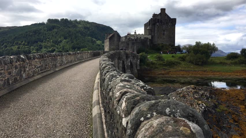 Crossing Loch Duich walking on the castle bridge Eliean Donan Castle. Lovely big cinematic view of the castle, bridge and surrounding lake, Scotland