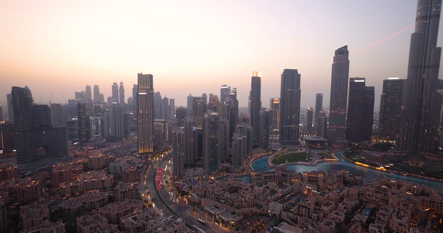 A beautiful tourist woman in a white dress holding a drink enjoys the evening view behind the modern skyline of Downtown Dubai, UAE