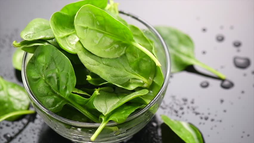 Spinach in a transparent glass bowl on gray background with reflection. Heap of Baby spinach fresh leaves close up with water drops, Healthy vegan food, diet, dieting, vitamin concept, rotation