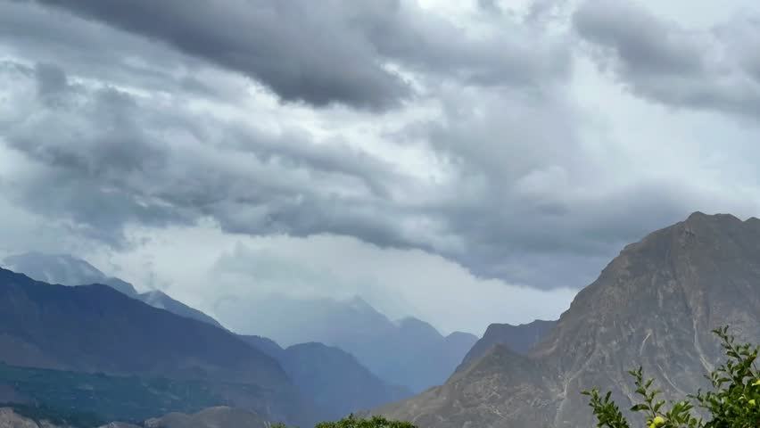 Timelapse shot capturing heavy, rainy clouds passing over range of mountains at Hunza, Pakistan during daytime.