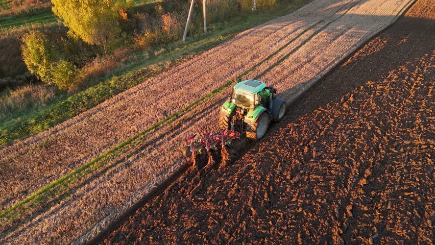 Aerial shot of a green tractor plowing a field during sunset, preparing the soil for planting.