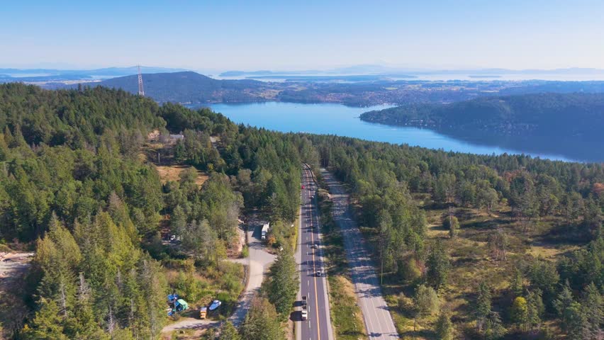 Expansive aerial view captures the picturesque Trans-Canada Highway winding through dense green forest towards the Saanich Inlet in Victoria, BC, Canada