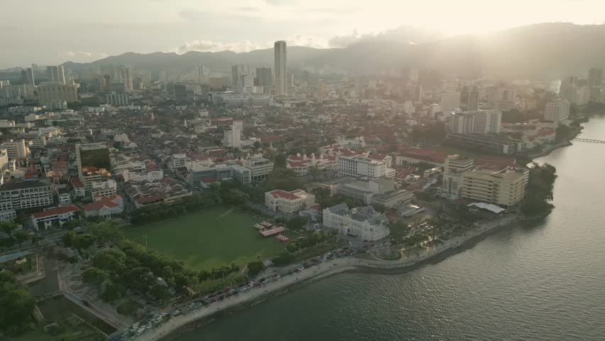 Aerial slow dolly over cityscape and coastline with green fields and historic buildings, vibrant urban setting, George Town Penang Island Malaysia