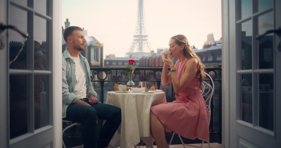 Romantic Proposal Unfolds on a Parisian Balcony as a Young Man Kneels with a Ring to Ask His Girlfriend to Marry Him. Eiffel Tower in the Background. Her Surprise Turns to Joy as She Accepts