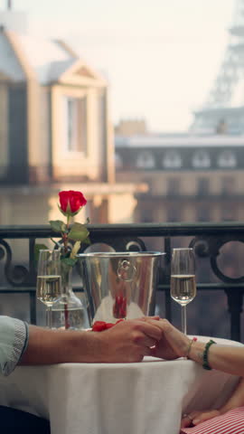 Vertical Screen: Champagne Glasses Clink in Celebration as a Couple Enjoys a Romantic Evening on a Paris Balcony. They Hold Hands Together. Eiffel Tower Stands in the Distance