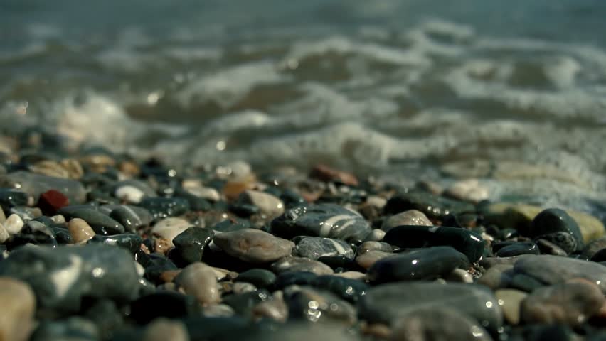 Wave Splashing Over Pebbles At Sea. Close Up Sea Ocean Beach In Slow Motion. Waves Crashing In Background And Wave Splashing Over Pebbles. Air Bubble On Pebbles. Vocation Or Summer Holiday Concept
