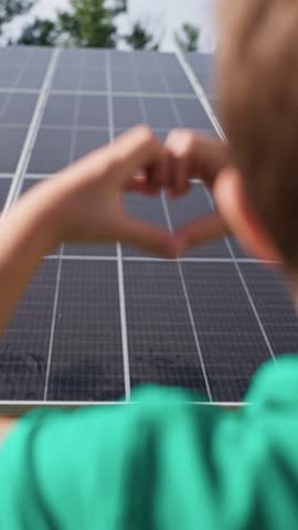 A child boy shows a heart with his hands on the background of solar panels. The concept of green eco electricity, future technological protection of environment and ecology, production of electricity