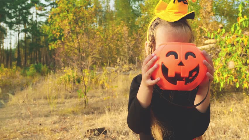 A girl in a carnival witch costume holds a bucket for candy. Trick or treat for Halloween takes candy. Childhood, traditions and fun concept. Slow motion