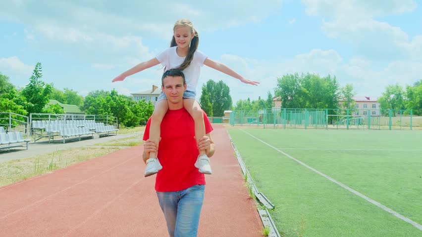 Father, daughter and piggyback fun in outdoor, adventure and play in sport ground for bonding or energy. Daddy, girl and plane game or flying together in outdoors, family and carrying kid for happines