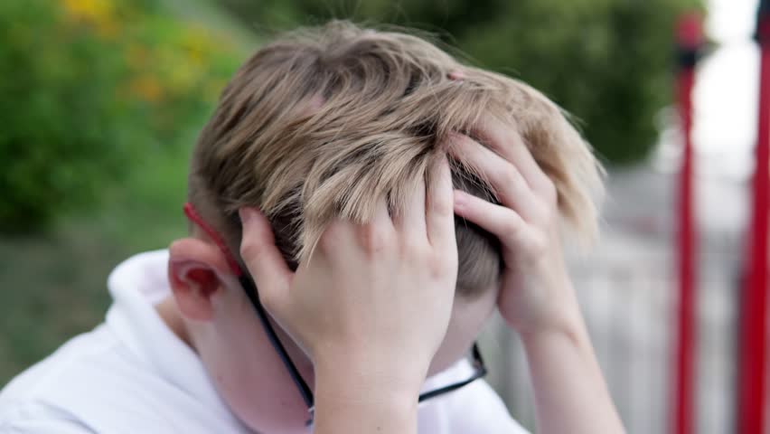 The boy feels a sharp headache while walking outside. School fatigue led to a migraine.