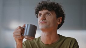 Dreamy man drinking coffee pondering project at home workplace closeup. Smiling remote employee sitting at living room. Happy curly entrepreneur thinking on business success at modern domestic office - Powered by Shutterstock - Get 15% off with code: PIKWIZARD15