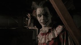 Crazy creepy killer man dressed as clown with makeup at attic in ruined house looks at camera smiles and walks away. Halloween thriller concept. - Powered by Shutterstock - Get 15% off with code: PIKWIZARD15