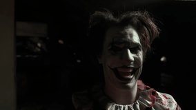 Crazy creepy killer man dressed as clown with makeup at attic in ruined house walks close at camera, smiling and laughing. Halloween thriller concept. - Powered by Shutterstock - Get 15% off with code: PIKWIZARD15