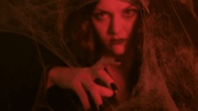 A dark-haired witch, with dramatic makeup, moves her hands as if casting a spell in warm, candlelit surroundings, with spider webs in the foreground. - Powered by Shutterstock - Get 15% off with code: PIKWIZARD15