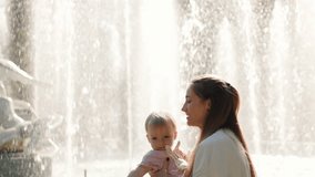 A mother joyfully lifts her toddler into the air near a fountain on a sunny day. The baby smiles and laughs, capturing a tender moment of play and affection between mother and child. - Powered by Shutterstock - Get 15% off with code: PIKWIZARD15