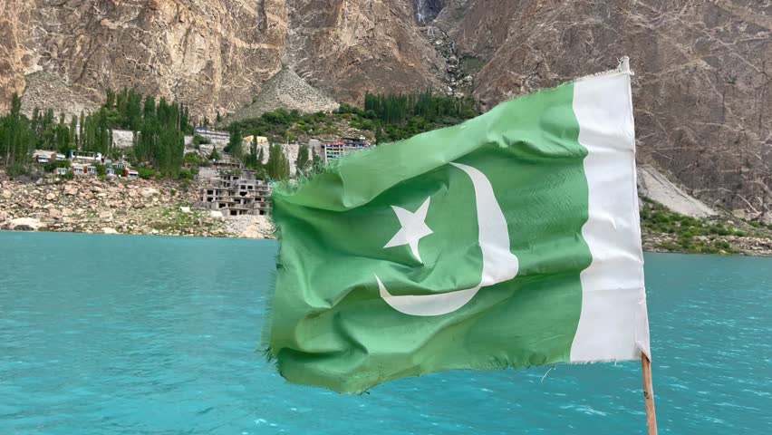 Pakistan flag gracefully flutters by the stunning Attabad Lake in the Gojal region of Gilgit-Baltistan, Pakistan, surrounded by rugged mountains and vibrant greenery.