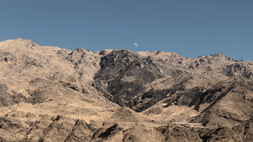 Aerial view of rugged, arid peaks of Andes with moon in blue sky. Tafí del Valle, Tucumán, Argentina.
