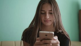 Attractive blonde Caucasian teen girl sitting on a sofa at home and texting on her phone. Smiling, laughing female. Love, friendship concept. - Powered by Shutterstock - Get 15% off with code: PIKWIZARD15