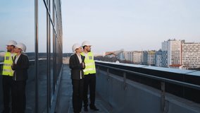 Construction professionals, man and woman, stand on rooftop, wearing hard hats and reflective vests. Man gestures outward, holding blueprints, while explaining progress or future plans for cityscape. - Powered by Shutterstock - Get 15% off with code: PIKWIZARD15