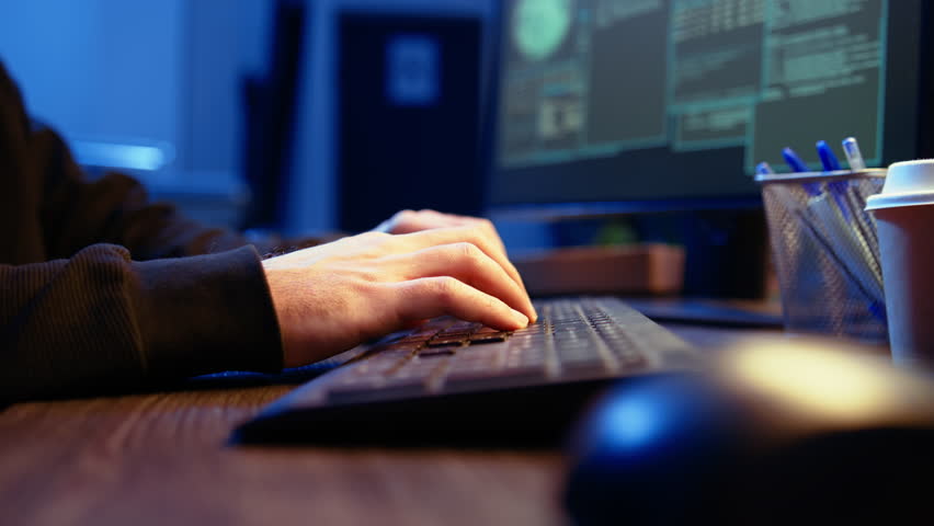 Hacker in secret underground shelter typing on keyboard, writing lines of code on computer, trying to get past security systems with virus. Scammer working on hacking script, camera A close up shot