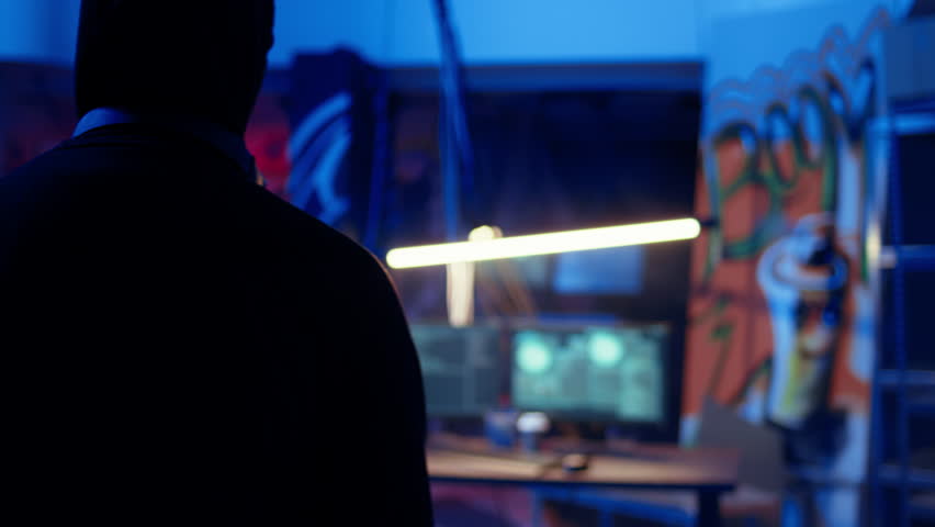 Hacker coming in secret base to use bugs and exploits to break into computer systems and access valuable data, bypassing firewalls, panning shot. Cybercriminal arriving in underground bunker