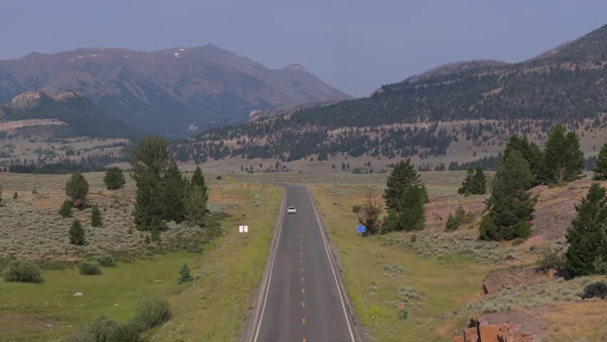 A car drives down a remote road through mountains and valleys on a sunny day in Wyoming