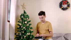 Brazilian man decorating a Christmas tree in his living room. The tree has gold ornaments and a star on top, with a window nearby - Powered by Shutterstock - Get 15% off with code: PIKWIZARD15