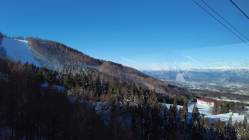 Aerial view from a scenic cable car flying over forests of frost trees on the snowy mountainside under sunny winter sky in Zao, a famous resort for skiing and Onsen (hot springs) in Yamagata, Japan