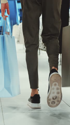 Closeup man walking through mall holding shopping bags, emphasizing movement and modern shopping experience. Concept of retail therapy and consumerism