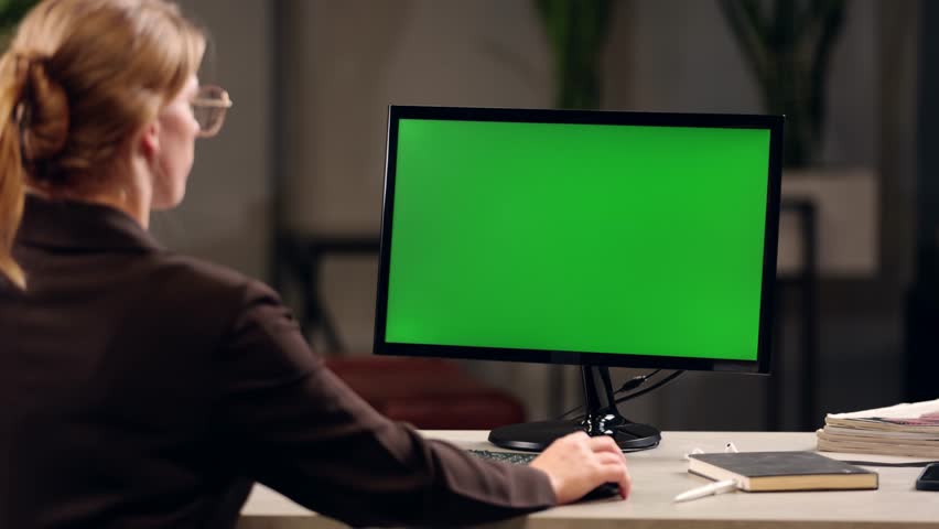 Young Woman Working In Office On Desktop Computer with Green Screen Mock Up Display. Over the Shoulder- Close-up of Monitor With Green Screen Chromakey