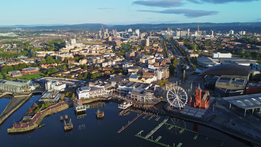 Aerial drone footage of Cardiff Bay area at sunrise, with the Cardiff city centre skyline visible in the distance. High angle left-to-right tracking shot.