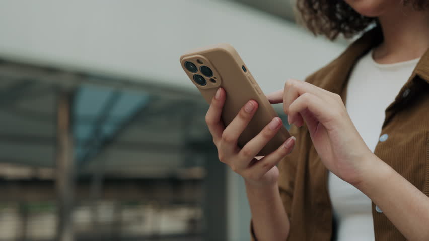 Close Up View of the Hands Holding Cell Phone and Chatting in Social Media while Standing Outdoors. Young Girl Going Outdoors and Texting Back on Telephone. People and Technology Concept