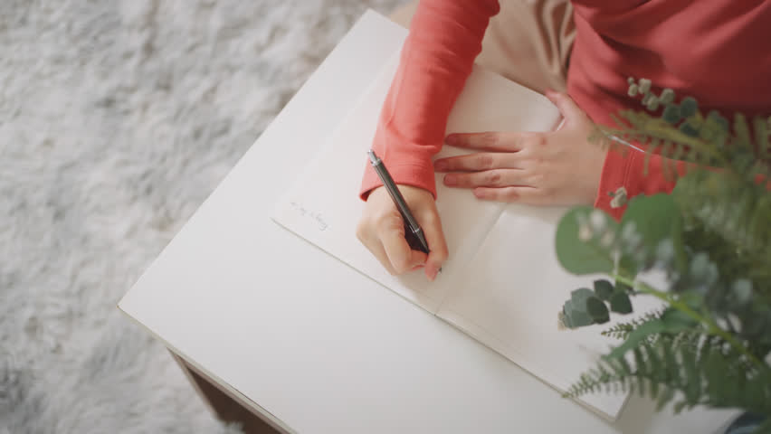 A person taking notes in a journal, highlighting focus, productivity, and the process of writing in a cozy home setting.