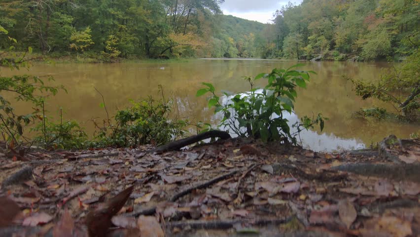 aerial footage of the silky brown waters of the Chattahoochee river surrounded by lush green trees and autumn colored trees with powerful storm clouds in Lithia Springs Georgia USA	
