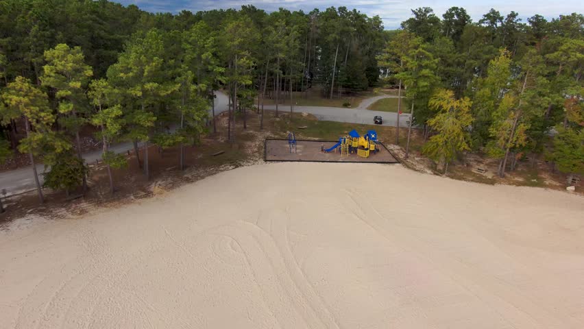 aerial footage of a blue and yellow jungle gym at the beach surrounded by silky brown sand and lush green trees at Lake Tobesofkee Recreation Area in Lizella Georgia USA