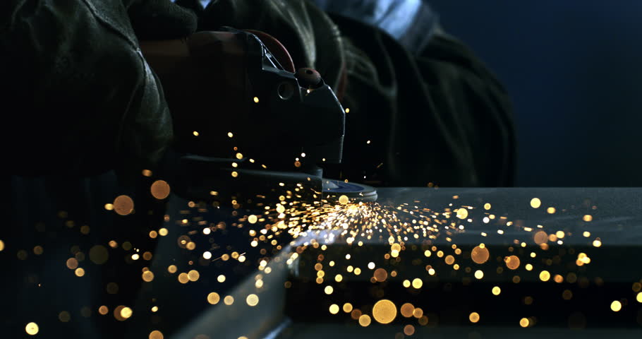 Super slow motion macro of blacksmith welder is smoothing metal steel with industrial angle grinder with flying sparks in workshop at 1000 fps.