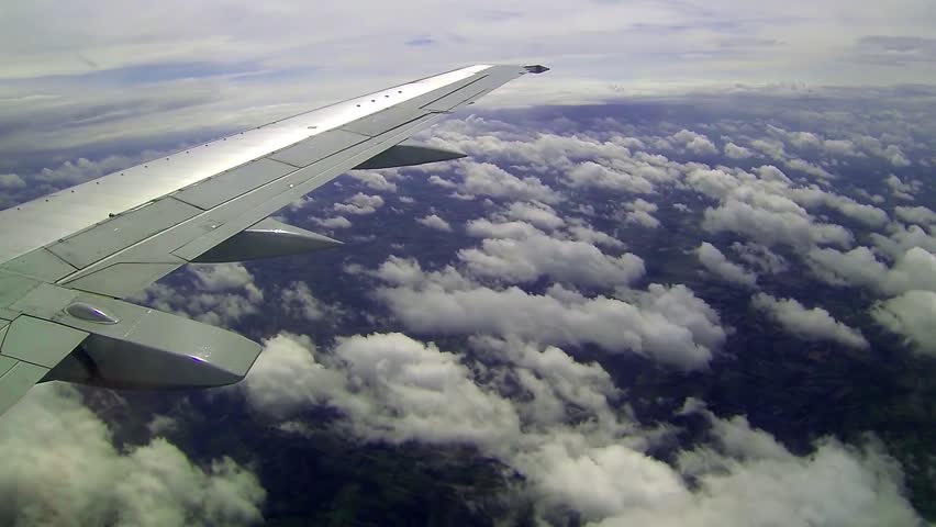 Commercial Passenger Airplane Flying Over Clouds. Airplane Window View of Wing in Flight with Beautiful Clouds Over the Land. Commercial Air Transportation. Air Travel - Background. Long-Haul Flight.