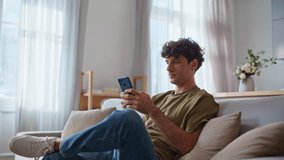 Home guy browsing cellphone application at soft couch. Handsome young man typing on smartphone screen sitting sofa at modern apartment. Smiling customer making online order using mobile phone app  - Powered by Shutterstock - Get 15% off with code: PIKWIZARD15