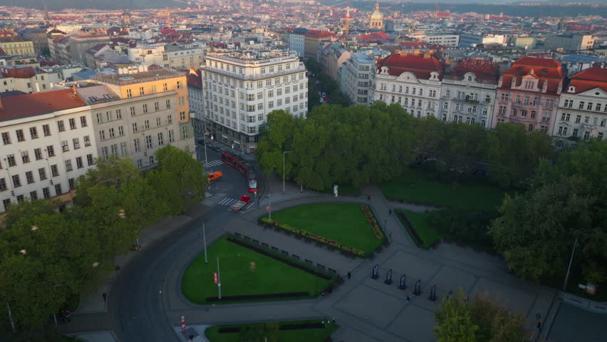 Aerial view of Prague at sunset. The camera pans over a park and buildings, showing the cityscape and the Petrin Hill in the background