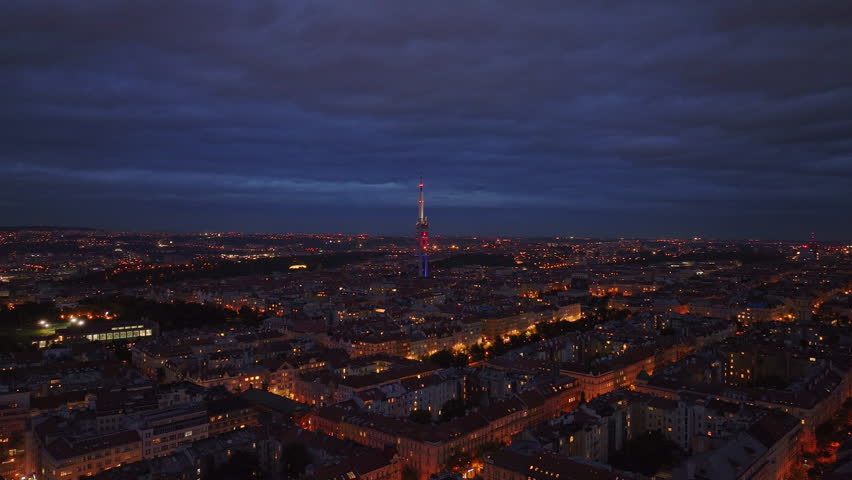 Aerial view of the city of Prague at dusk with clouds moving in the sky. The Zizkov Television Tower stands on the city