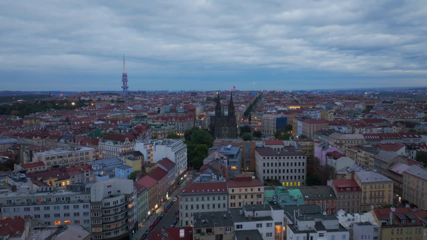 Prague slowly transitions from day to night in this aerial view overlooking the urban landscape. The Zizkov Television Tower is visible in the distance