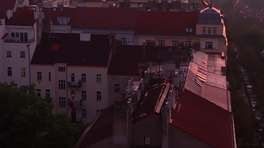 Smoke rises over the Prague skyline at sunset, bathing the city in a warm glow. Morning light highlights rooftops and historic architecture, creating a stunning urban landscape