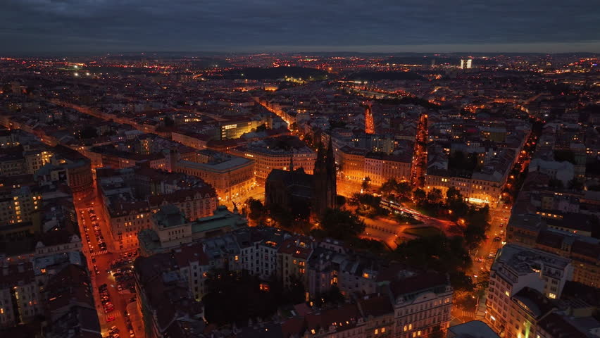 City lights illuminating as dusk settles on Prague, Czech Republic. This aerial view features the church of St. Henry and Kunhuta
