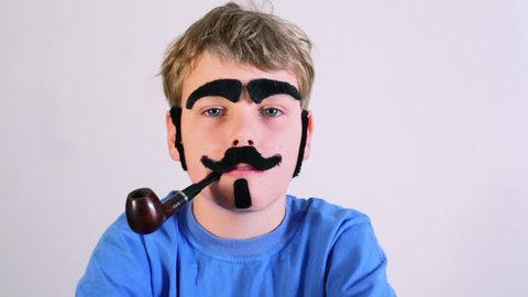 Little boy in blue shirt with pipe, fake mustache, eyebrows, beard and sideburns looks at camera