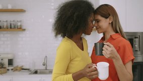 Happy interracial beautiful lesbian couple spend their free time together with love and affection in the kitchen at house. Lovely Black and White young female LGBTQ couple with cups of coffee at home. - Powered by Shutterstock - Get 15% off with code: PIKWIZARD15